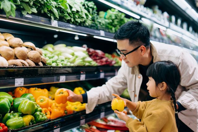 Asian dad helps young daughter choose pepper at grocery store