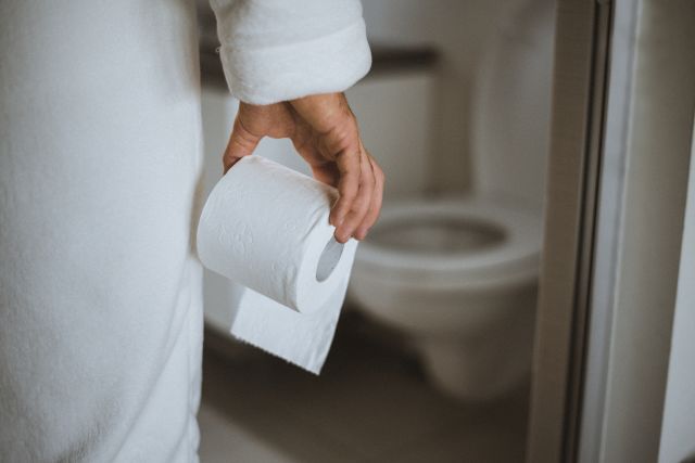 man in robe holding toilet paper walks into bathroom