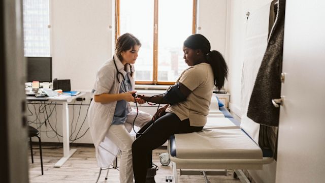 A healthcare provider checks blood pressure for a female patient during an appointment. Psoriasis is linked to a higher risk of cardiovascular disease.