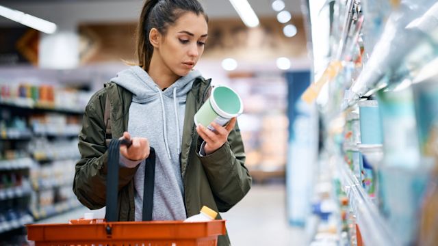 A woman reads a nutrition label on a container of yogurt while food shopping. Numerous foods are known to be common migraine triggers.