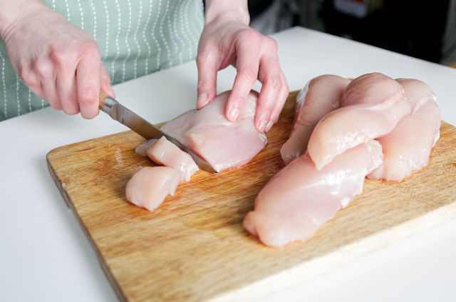 a person's hand cutting raw chicken breasts with a knife