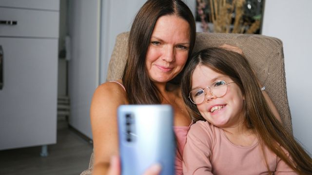 A mom and her young daughter with achrondoplasia take a selfie together at home.