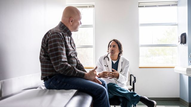 A senior man talks to his oncologist in an exam room.