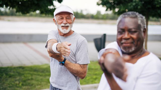 Two senior men stretch while exercising outdoors in a park.