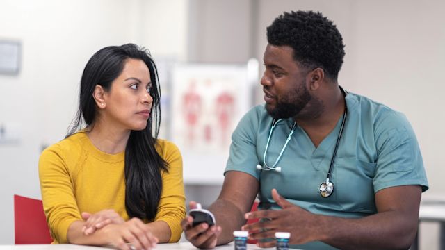 A male nurse teaches a younger woman with type 2 diabetes how to use a blood glucose meter.