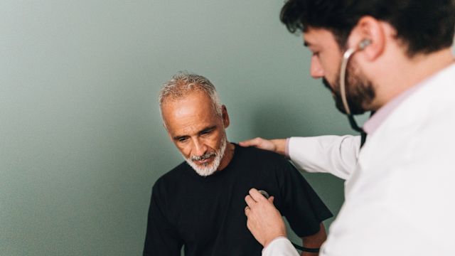 A healthcare provider uses a stethoscope to listen to the heart of a male patient in his 50s.