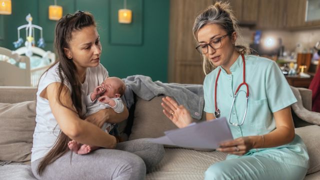 A mother of a newborn talks to a pediatrician during an appointment to discuss a diagnosis of achondroplasia.