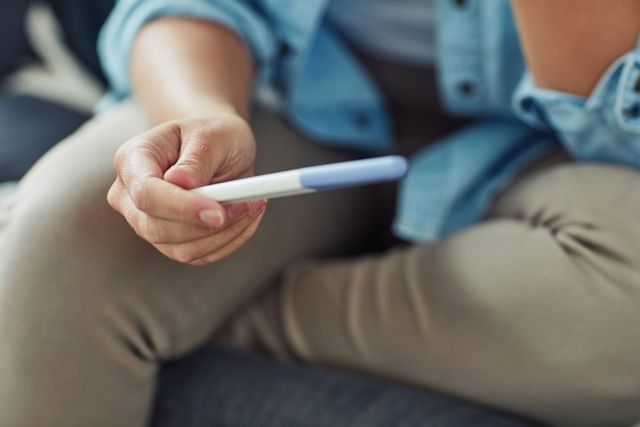 close up shot of someone sitting on a couch and looking at a home pregnancy test