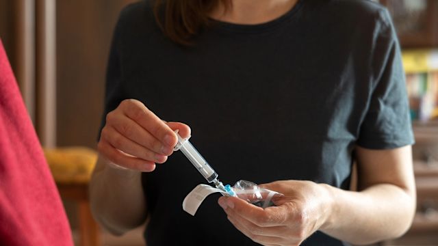 A caregiver opens a syringe to administer a dose of on-demand medication to a loved one who is experiencing an HAE attack that requires treatment.