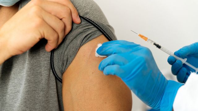 A pharmacist administers a COVID-19 vaccine into the upper arm of a male patient.