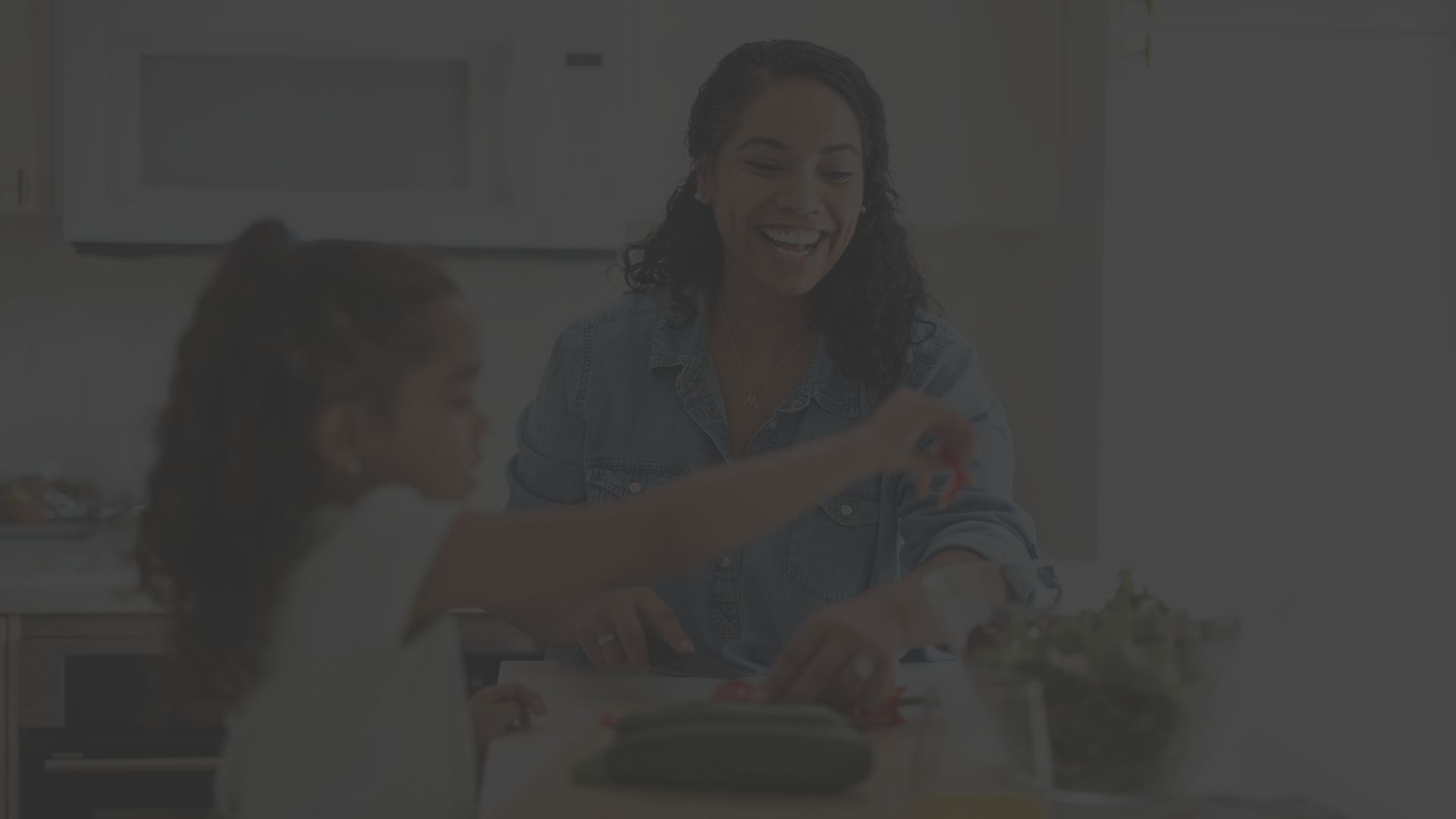 a woman and her daughter happily prepare fresh vegetables in a kitchen