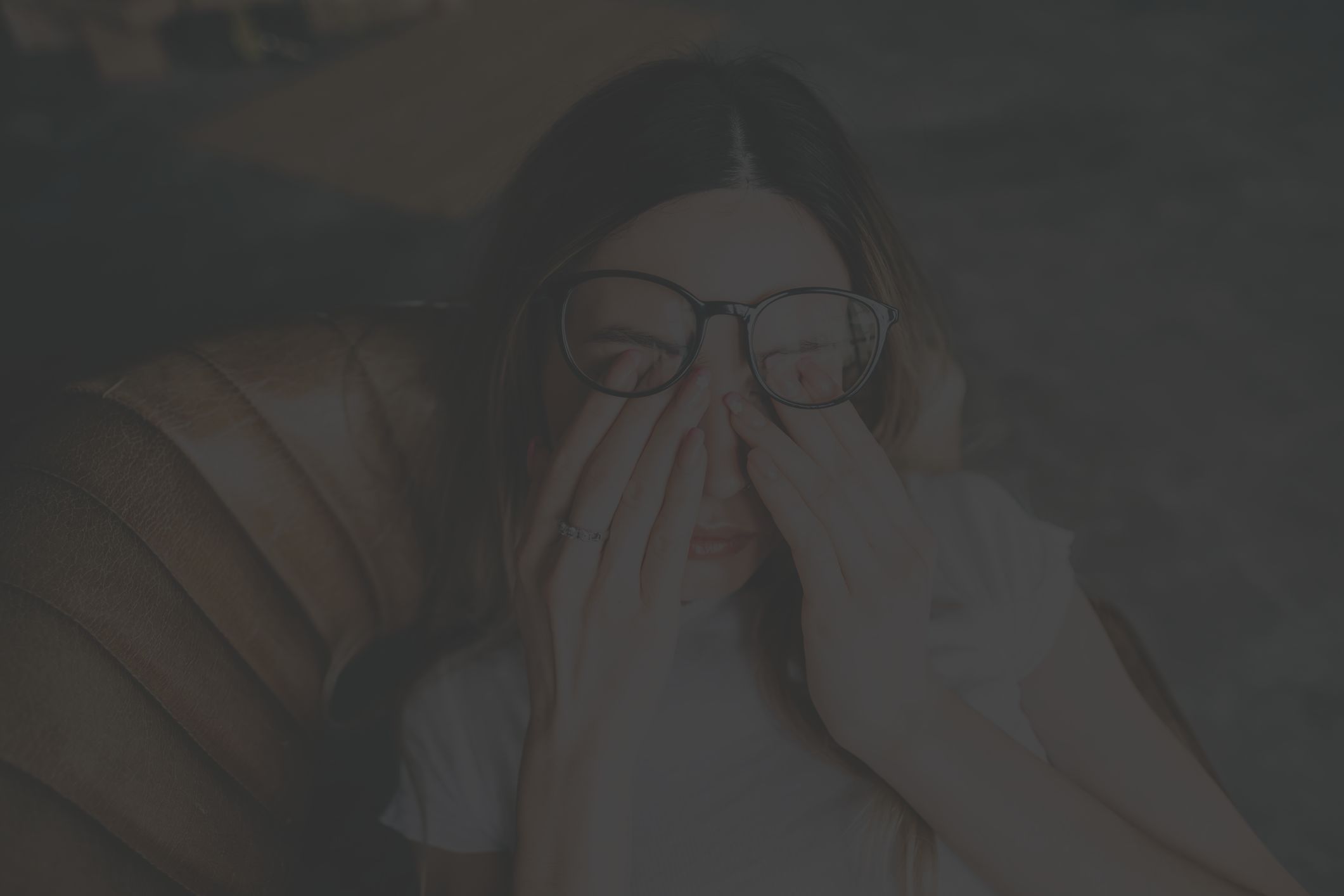 young woman lying back on couch, tired and rubbing her eyes