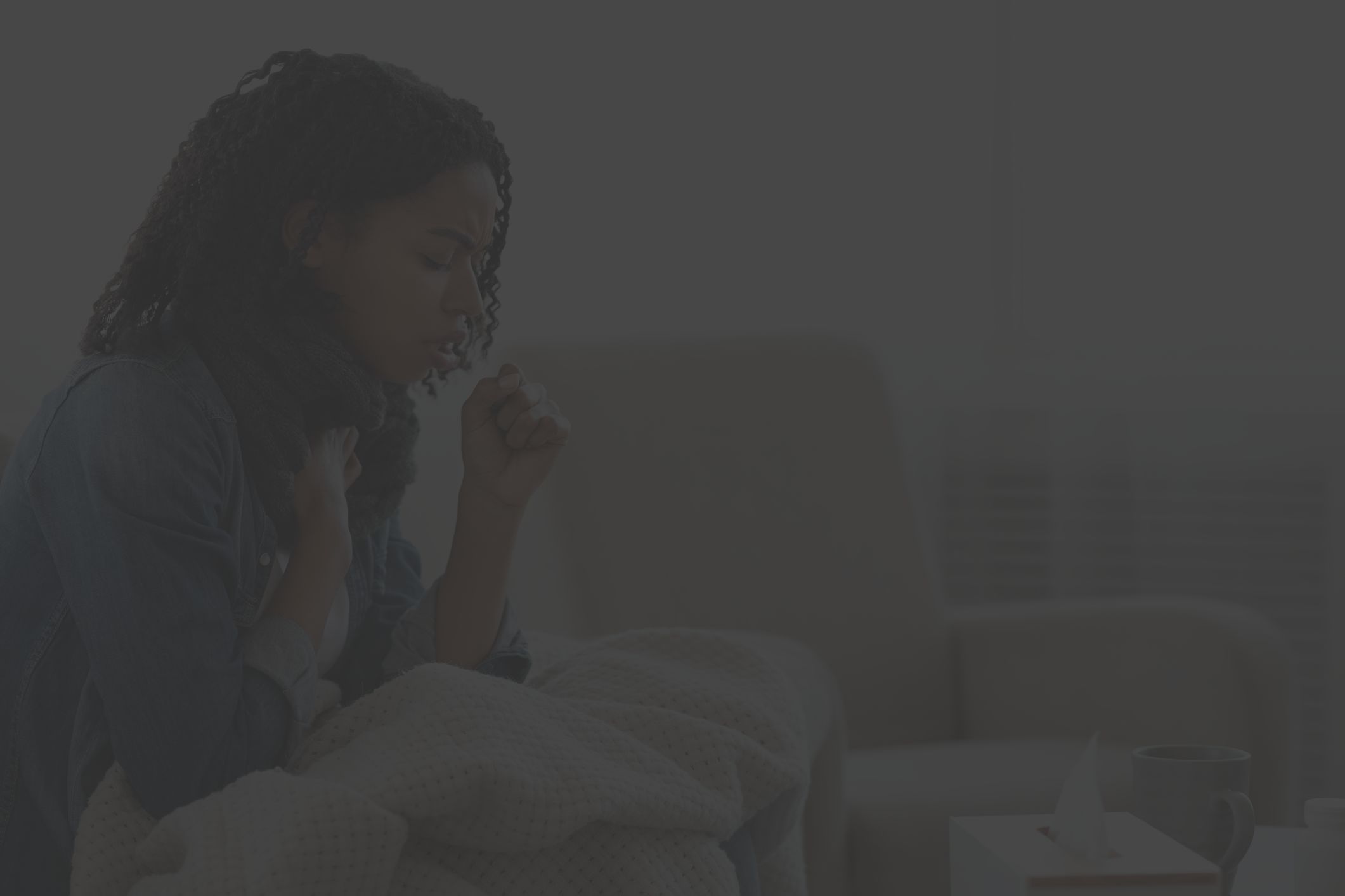 Black woman sitting on bed, sick with a cold or the flu and coughing