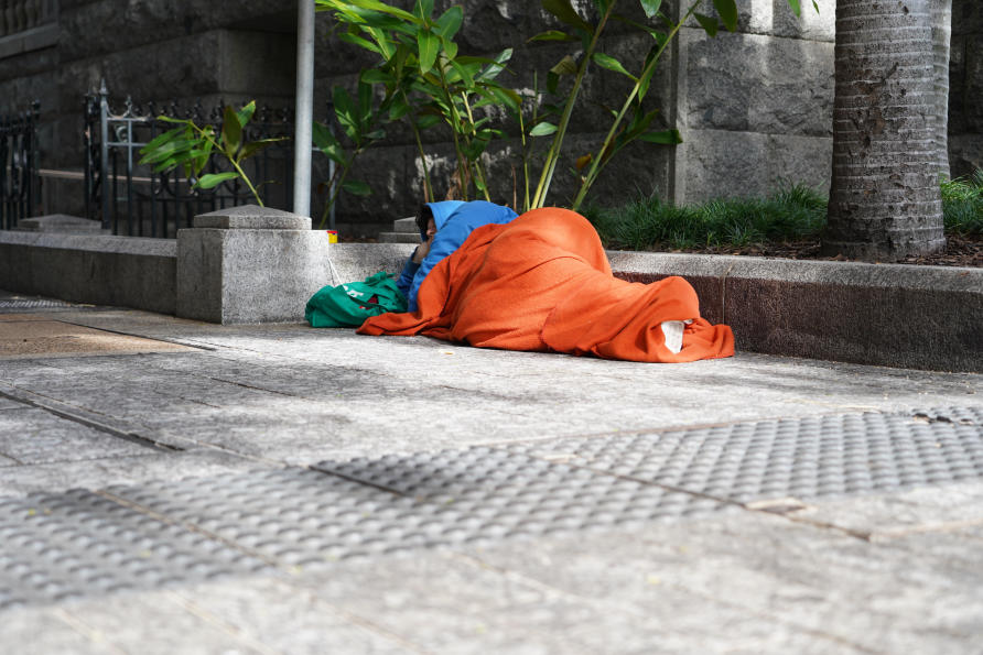 Person sleeping on a footpath wrapped in an orange blanket